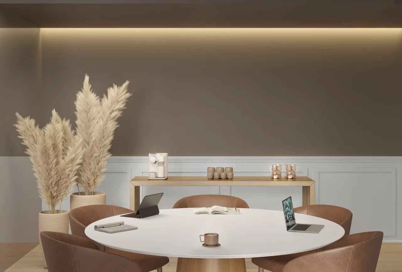 Sala de reuniões ou estudos com mesa redonda, cadeiras de couro e decoração em tons neutros.